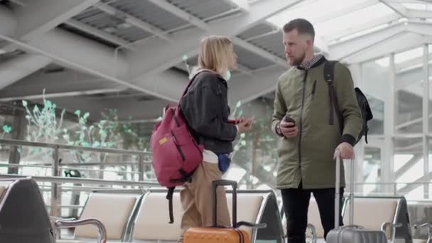 Manliga och kvinnliga resenärer kommunicerar i Hall of Airport, håller resväska — Stockvideo