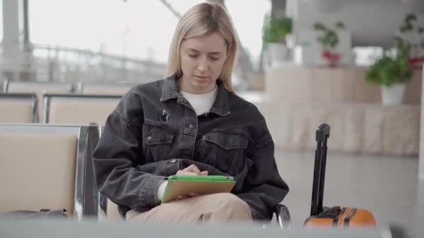 Frau checkt E-Mail per Tablet in Wartehalle des Bahnhofs, sitzt allein — Stockvideo