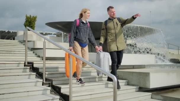 Felice giovane uomo e donna con valigie si stanno abbassando sulla scala sulla strada soleggiata — Video Stock