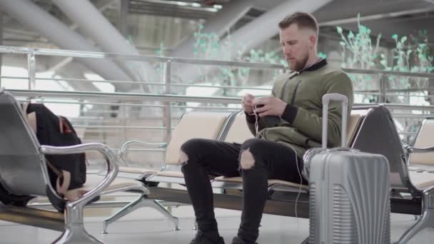 El joven está desenredando cables de auriculares, sentado en la estación terminal — Vídeos de Stock