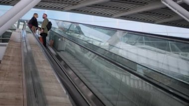 Bagajı olan bir çift yolcu yürüyen merdivende duruyor.