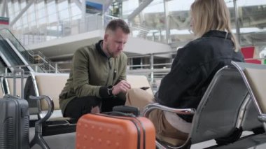 İki yolcu büyük salonda uçak ya da tren bekliyor, erkek ve kadın oturuyor