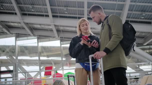 Călătorii sunt în picioare cu bagaje în interiorul sălii de aeroport, folosind smartphone-ul — Videoclip de stoc