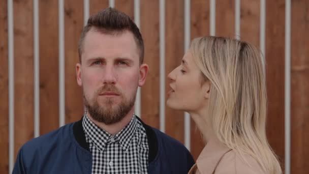 Pretty blonde woman is whispering on ear of handsome bearded man outdoors — Stock Video