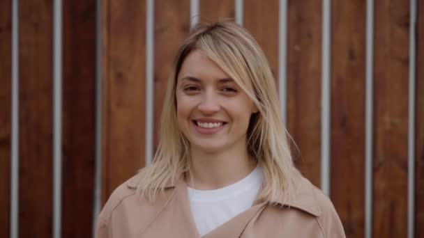 Heureuse jeune femme blonde regarde la caméra à l'extérieur et souriant — Video