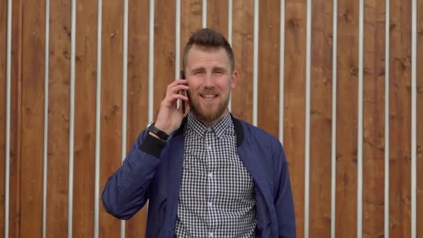 Knappe man praat door mobiele telefoon emotioneel, staande buitenshuis — Stockvideo