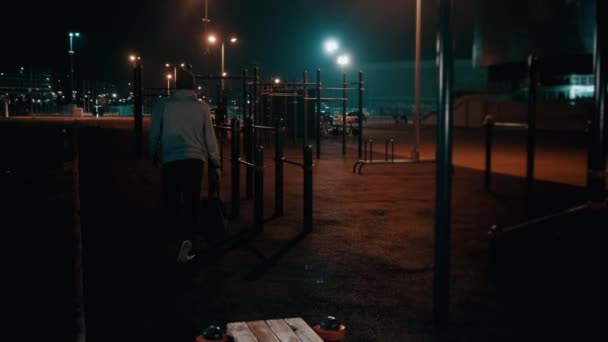 若い男が夜公園のスポーツ場から出て行く — ストック動画