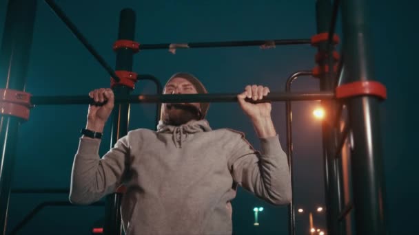 Hombre atlético está entrenando en la barra horizontal en la noche fría, hacer ejercicio — Vídeo de stock