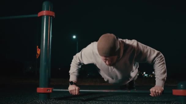 El hombre está haciendo flexiones al aire libre en la zona deportiva en la noche — Vídeo de stock