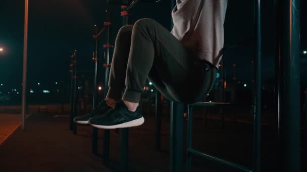 El hombre está entrenando los músculos abdominales levantando las piernas en la barra horizontal al aire libre — Vídeos de Stock