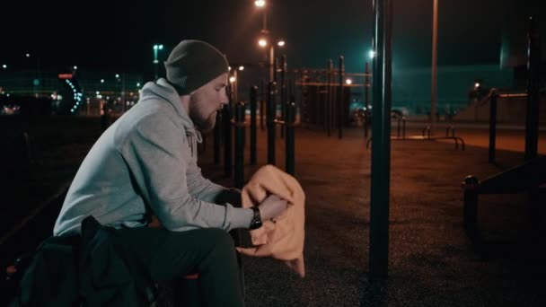 피곤한 남성 운동 선수는 밤에 야외 스포츠 그라운드에 타워에 의해 그의 얼굴을 닦고있다 — 비디오