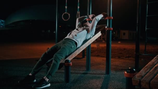 El hombre está acostado en equipo deportivo al aire libre en el parque y piernas de entrenamiento y abdomen — Vídeos de Stock