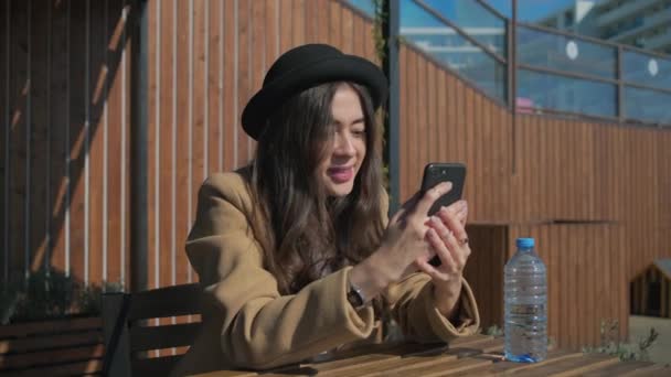 Chica conversadora en la mesa con un teléfono inteligente . — Vídeos de Stock