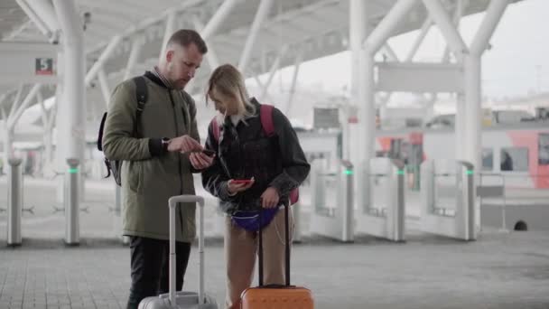 Casal em pé fora de um aeroporto com malas rolantes . — Vídeo de Stock