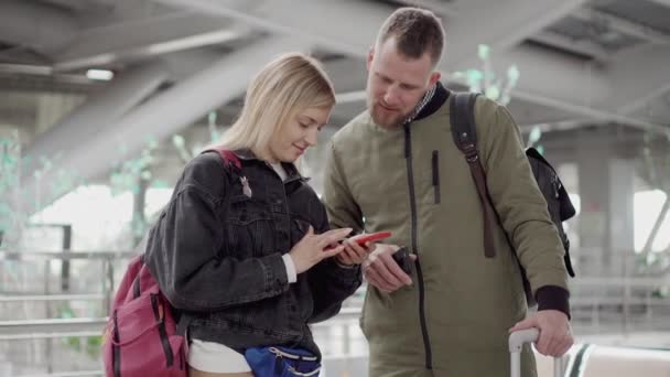 Mann spricht Frau an, während sie Smartphone am Flughafen benutzt. — Stockvideo