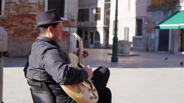 Italia, Venecia, febrero de 2019. Elegante músico callejero tocando la guitarra sentado en una silla vestida de negro . — Vídeo de stock