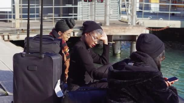 Italien, venedig, februar 2019. mehrere touristen sitzen mit gepäck auf einem peir und schauen auf ihre smartphones, digitale generation. — Stockvideo