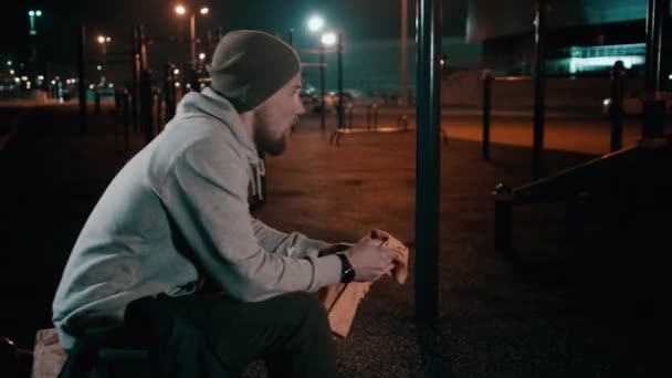 Guy sitting on a bench on sports ground. — Stock Video