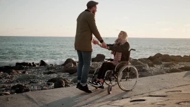 Hombre alegre está cogido de la mano de su novia discapacitada en el terraplén del mar — Vídeo de stock