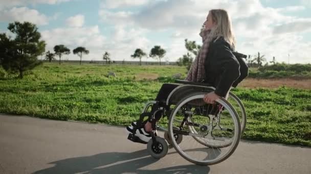 Young woman is sitting in invalid carriage and moving in park area — 图库视频影像