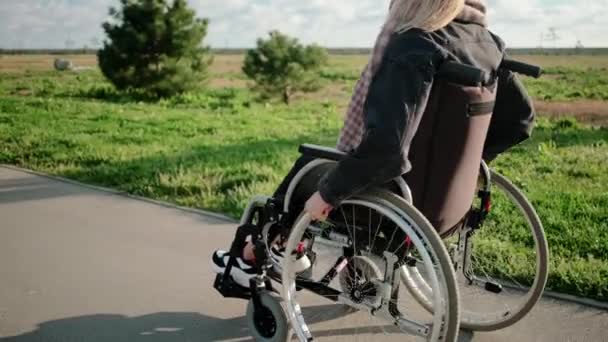 Ung kvinna rör sig på väg i parken ridning invalid stol i soligt väder — Stockvideo