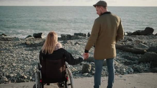 Пара-любовница стоит на берегу моря, инвалид и здоровый мужчина, вид сзади — стоковое видео