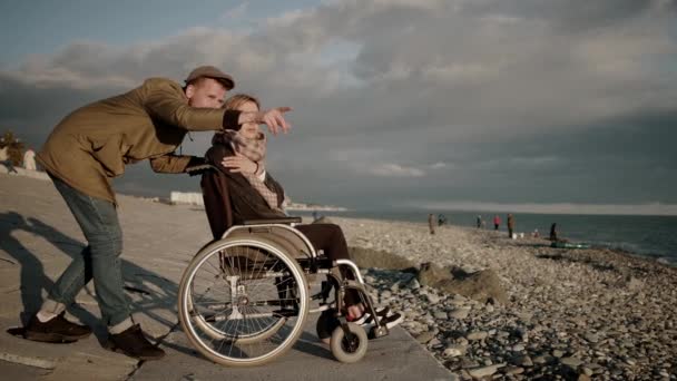 Mann umarmt seine Frau, die in ungültiger Kutsche auf einer Böschung sitzt — Stockvideo