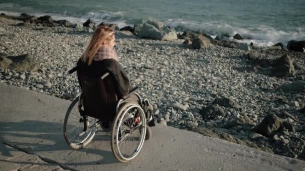 Woman with disabilities is sitting in invalid carriage and looking on sea — Stock video