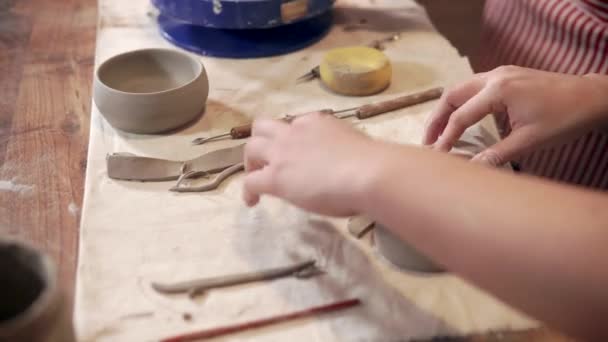 Woman is processing clay detail in workshop, close-up view of hands and table — Stock Video