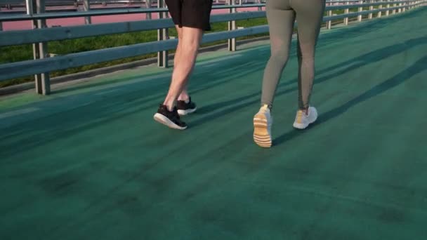 Πόδια ανθρώπου και γυναίκας που τρέχουν στο στάδιο του ανοιχτού αέρα, πίσω όψη — Αρχείο Βίντεο