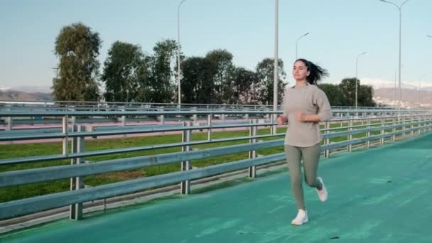 Chica delgada está trotando en pista de estadio en día soleado , — Vídeos de Stock