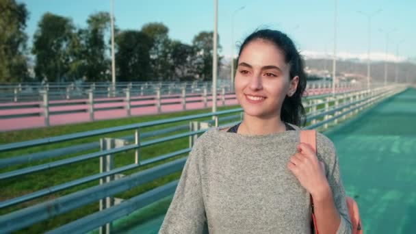 Щаслива молода спортсменка йде через трек відкритого стадіону і посміхається — стокове відео