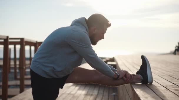 Bello sportivo uomo è stretching suo gambe su mattina allenamento all'aperto — Video Stock