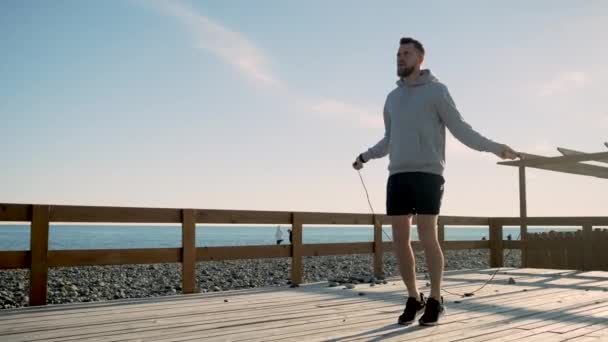 Stilig ung man tränar, hoppar rep på havsstranden — Stockvideo