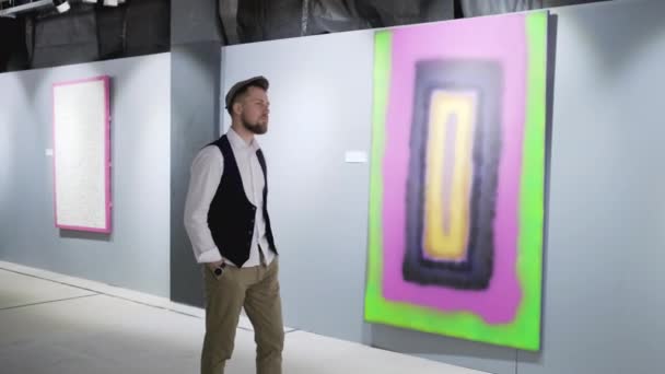 Männlicher Kunstliebhaber schlendert in Saal der Kunstgalerie und betrachtet Bilder — Stockvideo
