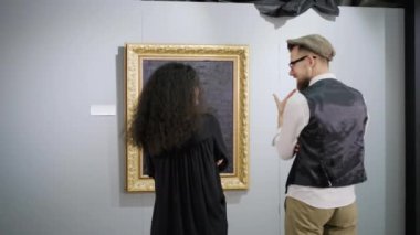 Modern sanat sergisi ziyaretçi çifti resimlerin önünde sohbet ediyor