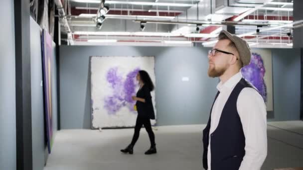 People are examining pictures in hall of modern art gallery, man and woman — Stock Video