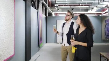 Erkek ve kadın şampanya içiyor ve modern sanat galerisinde resim leniyor