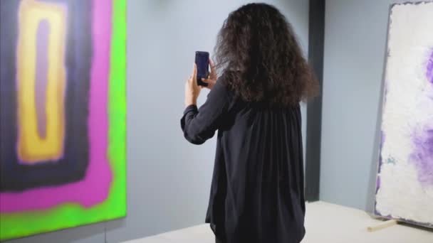 Female guest of art gallery is taking photo of picture by smartphone — Stock Video