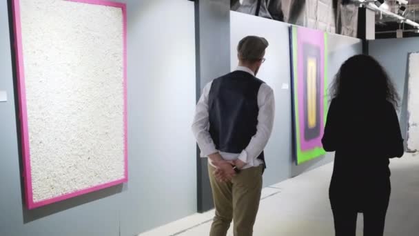 Muž a žena se pohybují v galerii umění a mluví o obrázcích — Stock video