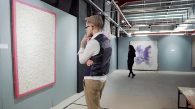 Erkek ziyaretçi sergide modern soyut sanatçının resim çalışmalarını inceliyor