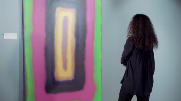 Młoda brunetka kobieta rozważa jasny abstrakcyjny obraz współczesnego artysty — Wideo stockowe