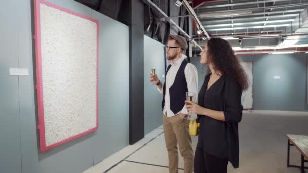 Dois jovens visitantes da exposição estão bebendo champanhe e vendo obras de arte da moda — Vídeo de Stock