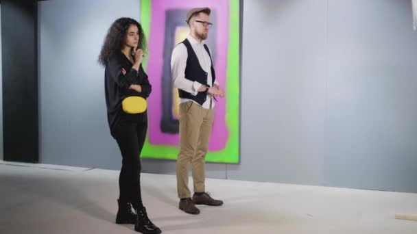 Bored man and woman are standing in front of abstraction picture in gallery — Stock Video