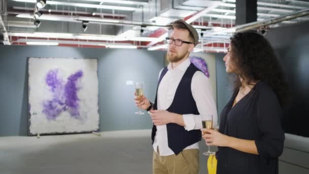 Пара посещает выставку абстрактных картин в музее, разговаривает в зале — стоковое видео