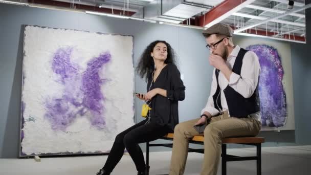 Dva Milovníci umění si užívají moderního výtvarného díla v galerii a poslouchají audio průvodce — Stock video