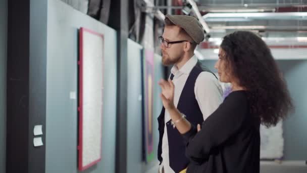 Twee jonge bezoekers van de kunsttentoonstelling bespreken een foto in een hal — Stockvideo