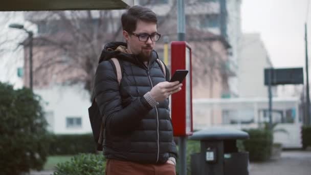 Homem é tela de rolagem de telefone celular na estação de ônibus — Vídeo de Stock