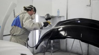Adam profesyonel fıskiye kullanarak siyah boya ile otomobilin bir kısmını kaplar.