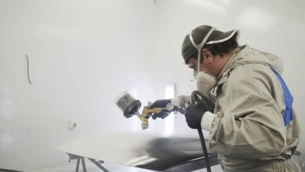 Художник работает в лакокрасочной кабине автосервиса, раскрашивает автодетали — стоковое видео